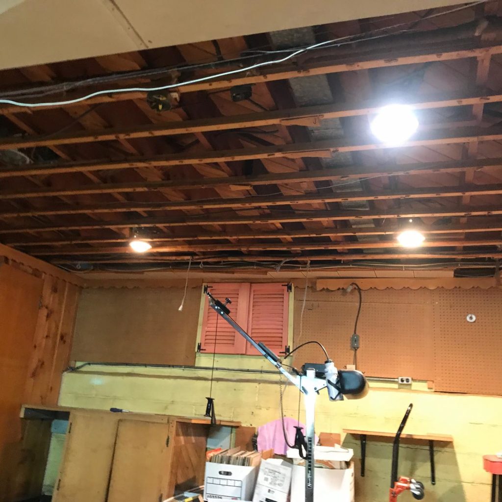 Basement with exposed ceiling beams, recessed lighting, wall paneling, and various stored items.